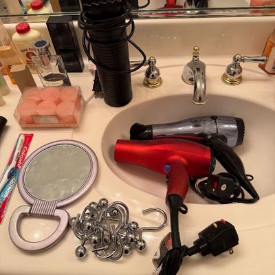 Sale Photo Thumbnail #171: Assorted bathroom accessories and personal care items, including a red Revlon hair dryer, a silver hair dryer, a hand mirror, and metal shower curtain rings.
