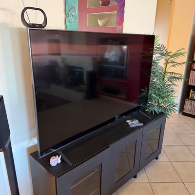 Large flat-screen television on a black media console with glass-front doors, accompanied by a digital antenna.