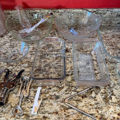Sale Photo Thumbnail #219: Assorted glassware including mixing bowls, loaf pans, and a cut-glass serving bowl, shown alongside kitchen utensils like corkscrews and a nutcracker.