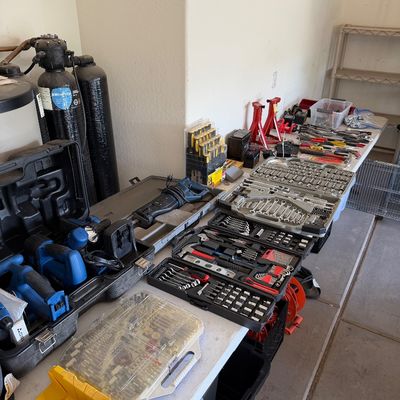 Assorted hand tools, power tools, and socket sets arranged on a folding table in a garage.