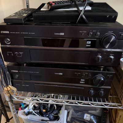 Two Yamaha Natural Sound AV Receivers, model RX-V1000, stacked on a wire shelf with remotes and assorted cables.