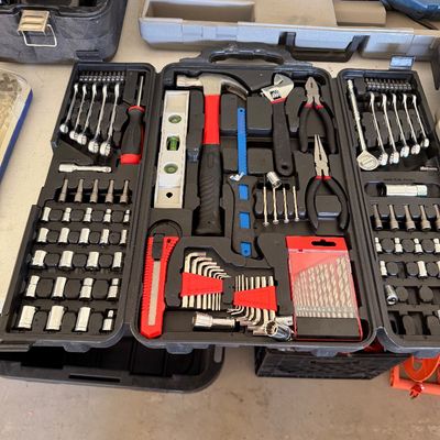 Comprehensive hand tool set in a black plastic folding carrying case, featuring a hammer, level, pliers, wrenches, sockets, and drill bits.
