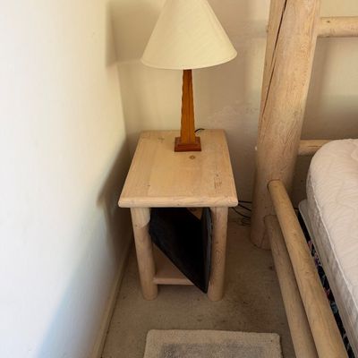 Sale Photo Thumbnail #195: Rustic log-style wooden nightstand with a lower shelf, paired with a slender wooden table lamp and cream shade.
