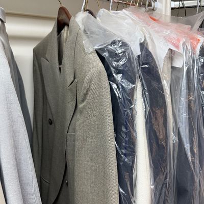 Sale Photo Thumbnail #113: Selection of men's suits and jackets hanging in a closet, including a double-breasted grey textured blazer and several garments protected in plastic dry cleaning bags.