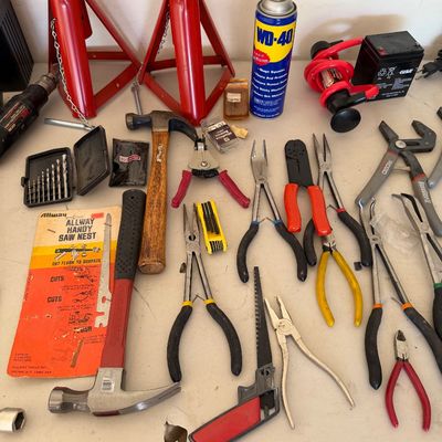 Assorted hand tools and garage items, including hammers, various pliers, a drill bit set, jack stands, and a can of WD-40.