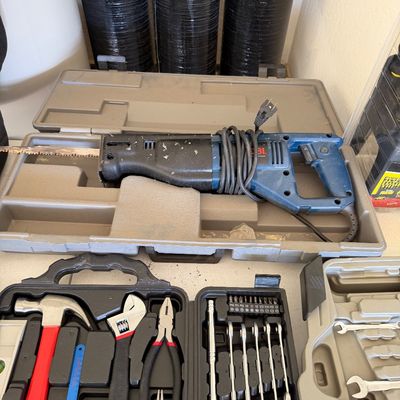 Ryobi corded reciprocating saw in its original plastic carrying case, shown alongside various hand tool sets including a hammer, pliers,...
