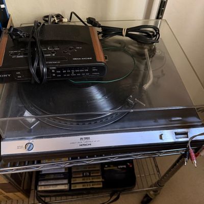 Hitachi HT-350 Uni-Torque direct drive turntable with a clear dust cover, shown with a vintage Sony Dream Machine clock radio resting on...