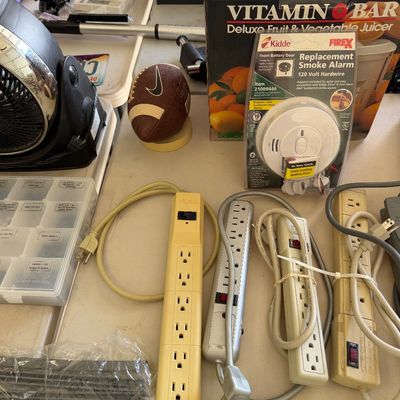 Sale Photo Thumbnail #102: Assorted household items including multiple power strips, a Kidde replacement smoke alarm in its original packaging, a boxed Vitamin Bar juicer, and a miniature Nike football.