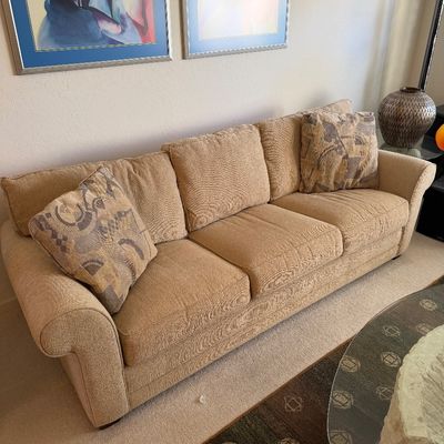 Sale Photo Thumbnail #320: Three-cushion beige textured fabric sofa with rolled arms, accompanied by two patterned accent pillows.