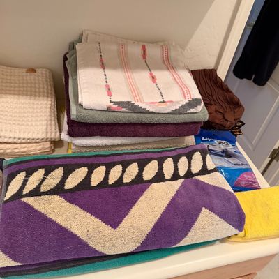 Sale Photo Thumbnail #169: Assorted bath and hand towels, including a purple and teal geometric patterned towel and a stack of solid and patterned linens.