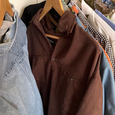 Sale Photo Thumbnail #155: Selection of men's vintage shirts and jackets hanging on a closet rod, featuring a brown Brandini button-down shirt and a light-wash denim jacket.