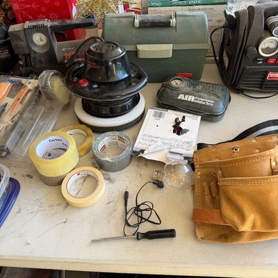 Assorted garage and workshop items, including a leather tool belt, rolls of tape, a car buffer, air compressors, and a green plastic...