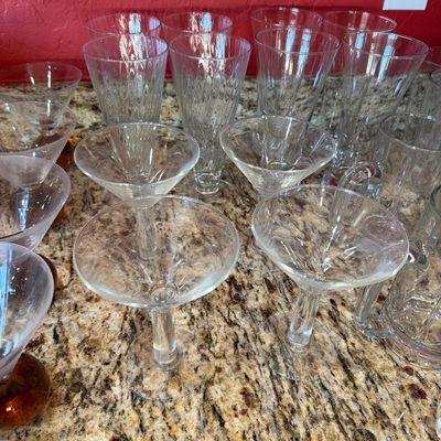 Sale Photo Thumbnail #208: Assorted clear glassware including martini glasses, tall pilsner-style glasses, and glass mugs, displayed on a granite countertop.