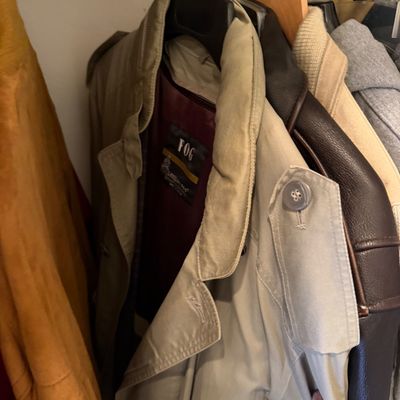 Sale Photo Thumbnail #177: Vintage London Fog trench coat in tan with a maroon lining, hanging in a closet alongside other outerwear.