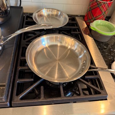 Sale Photo Thumbnail #118: Two stainless steel frying pans sitting on a black gas stovetop, showing light wear from use.