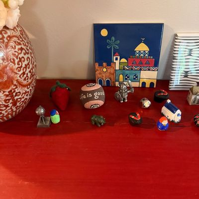 Sale Photo Thumbnail #76: Assortment of small decorative items and miniatures, including a hand-painted ceramic tile, a "Life is Good" ball, a strawberry pincushion, and various tiny figurines displayed on a red surface.