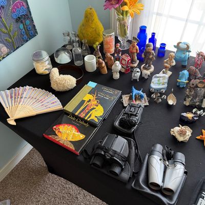 Sale Photo Thumbnail #95: Assortment of collectibles on a black tabletop, including Dale Chihuly art books, binoculars, a folding fan, small figurines, and vintage glass bottles.