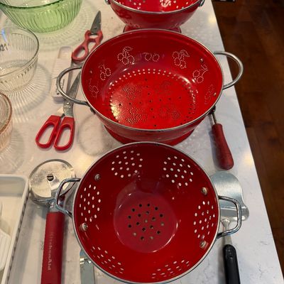 Sale Photo Thumbnail #129: Three vintage red enamel colanders with chrome handles, including one with cherry-shaped drainage holes, displayed alongside various kitchen utensils.