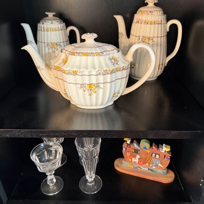 Sale Photo Thumbnail #197: Vintage Spode 'Buttercup' pattern tea and coffee pots displayed on a shelf alongside crystal stemware and a small wooden Noah's Ark figurine.