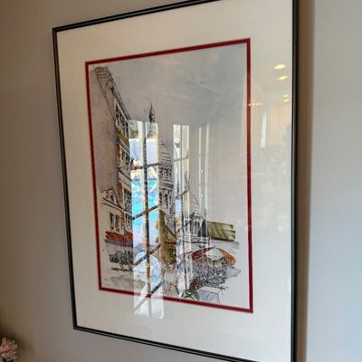 Sale Photo Thumbnail #178: Framed watercolor and ink illustration depicting a European street scene with a domed cathedral, double-matted with a red accent border in a dark metal frame.