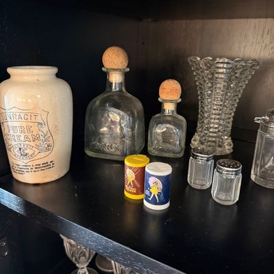 Sale Photo Thumbnail #185: Assorted vintage glassware and kitchen collectibles, including a Dunragit Pure Cream stoneware crock, Patron bottles with corks, miniature Morton Salt and Pepper shakers, and a clear hobnail glass vase.