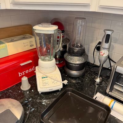 Sale Photo Thumbnail #119: Assorted kitchen small appliances including a vintage Krups blender, a NutriBullet, a red KitchenAid stand mixer, and a Cuisinart immersion blender on a granite countertop.