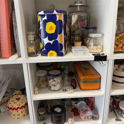 Sale Photo Thumbnail #50: Assorted vintage sewing and craft supplies, including buttons, thread spools, and notions stored in glass jars and decorative tins on white shelving.