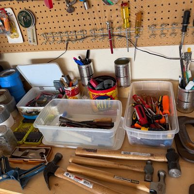 Sale Photo Thumbnail #106: Assorted hand tools and workshop supplies, including hammers, screwdrivers, and storage bins, arranged on a workbench with a pegboard background.