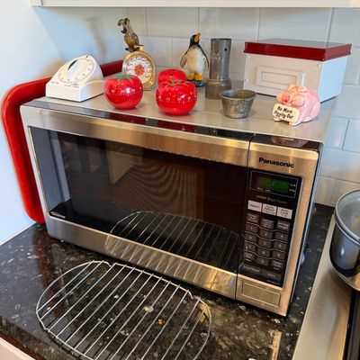 Sale Photo Thumbnail #110: Panasonic Inverter 1200W countertop microwave in stainless steel, shown with an assortment of kitchen timers and small decorative items on top.