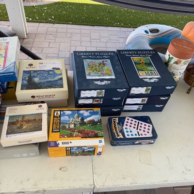 Sale Photo Thumbnail #161: Collection of jigsaw puzzles, including Liberty Puzzles and Wentworth wooden puzzles, alongside a vintage-style dominoes tin on a folding table.