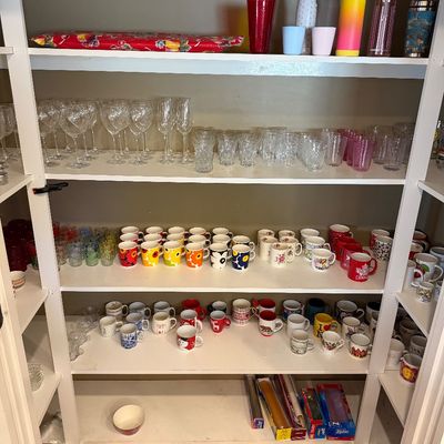Sale Photo Thumbnail #156: White pantry shelves filled with glassware, including wine glasses and tumblers, alongside a large collection of colorful ceramic coffee mugs.