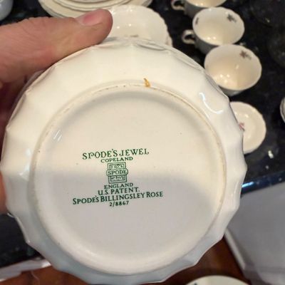 Sale Photo Thumbnail #138: Underside of a Spode's Jewel Copeland "Billingsley Rose" pattern bowl, showing the green maker's mark and patent details, with other matching dinnerware pieces visible in the background.
