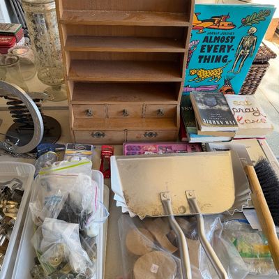 Sale Photo Thumbnail #100: Assorted household items including a vintage wooden spice rack or knick-knack shelf with drawers, a metal dustpan with brush, various books, and bins of craft supplies and hardware.