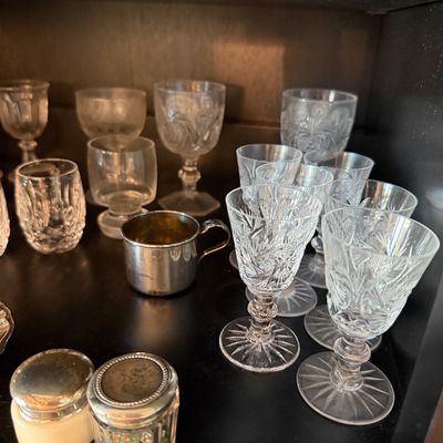 Sale Photo Thumbnail #189: Assortment of vintage crystal and cut glass stemware, including cordial glasses and goblets, displayed alongside small metal and glass vanity jars.