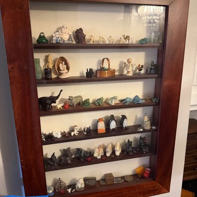 Sale Photo Thumbnail #30: Wall-mounted wooden shadow box display case with a glass front, filled with an assortment of miniature figurines including animals, people, and decorative objects.