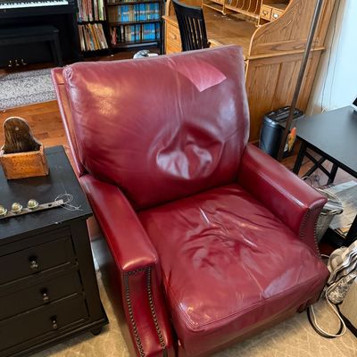 Sale Photo Thumbnail #218: Burgundy leather armchair featuring brass nailhead trim along the front arms, showing some wear on the seat and back cushions.