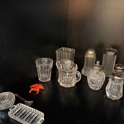 Sale Photo Thumbnail #182: Collection of vintage clear pressed glass tableware, including salt and pepper shakers, a small pitcher, a tumbler, and a miniature tray, displayed alongside a small orange frog figurine.