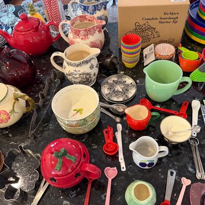 Sale Photo Thumbnail #140: Assortment of kitchenware and baking supplies, including a TeeMars sourdough starter kit, colorful measuring spoons, silicone baking cups, and various ceramic pitchers and bowls.