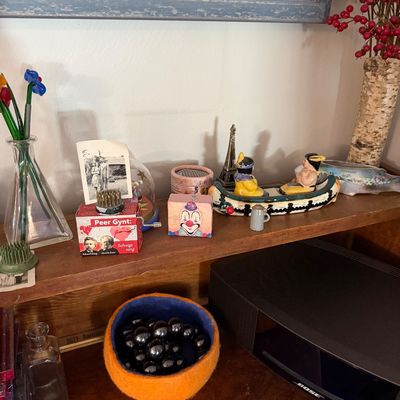 Sale Photo Thumbnail #78: Assorted vintage collectibles and decor on a wooden shelf, including a Peer Gynt music box, a miniature canoe figurine, a Bose speaker, and various small trinkets.
