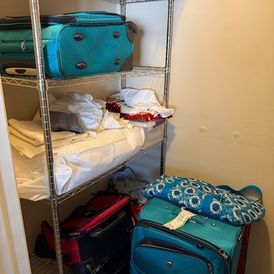 Sale Photo Thumbnail #13: Assorted soft-sided rolling luggage in teal and red, shown alongside folded linens on a chrome wire shelving unit.