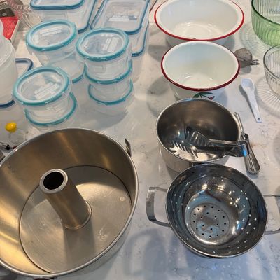 Sale Photo Thumbnail #128: Assorted kitchenware including an aluminum angel food cake pan, a stainless steel colander, enamel mixing bowls, and various plastic food storage containers.