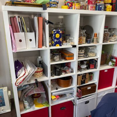 Sale Photo Thumbnail #49: White cube shelving unit filled with crafting supplies, vintage tins, storage jars, and fabric, alongside a sewing machine.