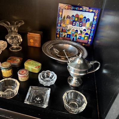 Sale Photo Thumbnail #175: Assortment of vintage collectibles including small pressed glass salt cellars, a silver-plated lidded condiment pot with spoon, vintage tins, and a colorful Jerusalem ceramic tile plaque.