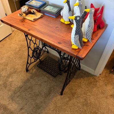 Sale Photo Thumbnail #17: Vintage Singer sewing machine base repurposed into a console table with a stained wood top, displaying various small decor items including fabric penguins and framed pictures.