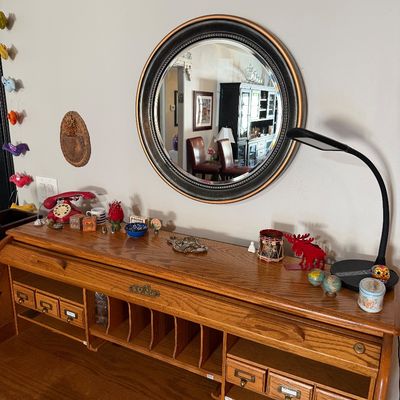Sale Photo Thumbnail #211: Oak roll-top desk organizer with cubbies and small drawers, paired with a round wall mirror featuring a black and gold frame.