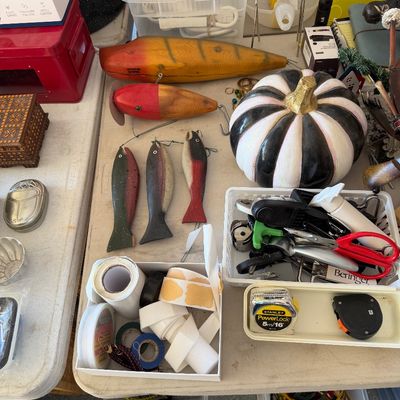 Sale Photo Thumbnail #102: Assortment of vintage wooden fishing lures, a black and white striped decorative pumpkin, and various household tools and tape on a folding table.