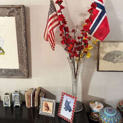 Sale Photo Thumbnail #206: Assorted home decor items including a tall crystal vase with faux red blossoms and flags, framed dog photos, small books, and decorative ceramic pieces on a dark tabletop.