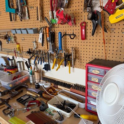 Sale Photo Thumbnail #105: A well-organized workshop pegboard and workbench featuring various hand tools, clamps, a small parts organizer, and a white Lasko desk fan.
