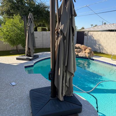 Sale Photo Thumbnail #166: Pair of large cantilever patio umbrellas with heavy-duty square bases, shown folded beside a swimming pool.
