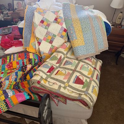 Sale Photo Thumbnail #9: Collection of handmade patchwork quilts in various colorful patterns, including a teacup motif and geometric designs, displayed on a bed.